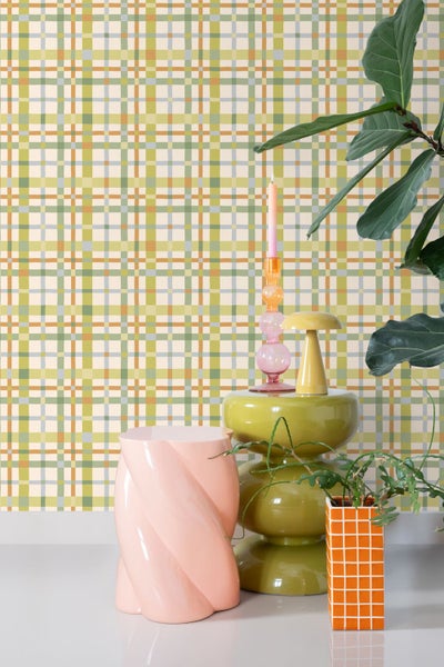 Vliestapete mit Karomuster in Grün und Orange, kombiniert mit modernen Dekorationsobjekten wie Kerzenständern und Zimmerpflanzen.