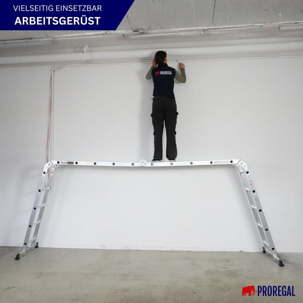 Eine Person steht auf einem Aluminium-Arbeitsgerüst vor einer Wand.