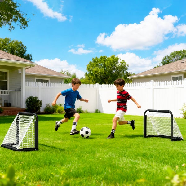 Zwei Kinder spielen Fußball auf einer Rasenfläche im Garten mit kleinen Fußballtoren.