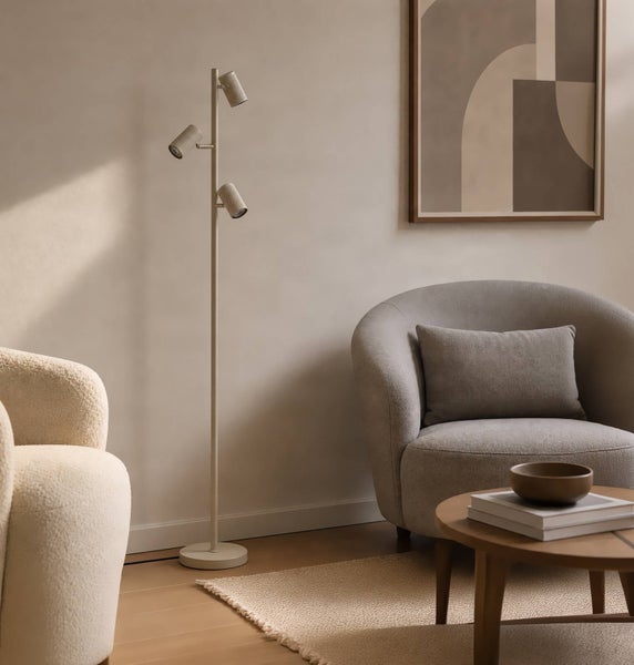 Moderne Stehleuchte mit drei verstellbaren Strahlern in einem hellen Wohnzimmer mit Sesseln und Couchtisch.