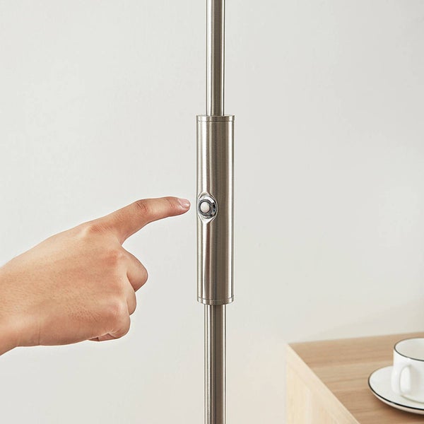 Ein Finger betätigt den Druckschalter an einer Stehlampe aus gebürstetem Metall.
