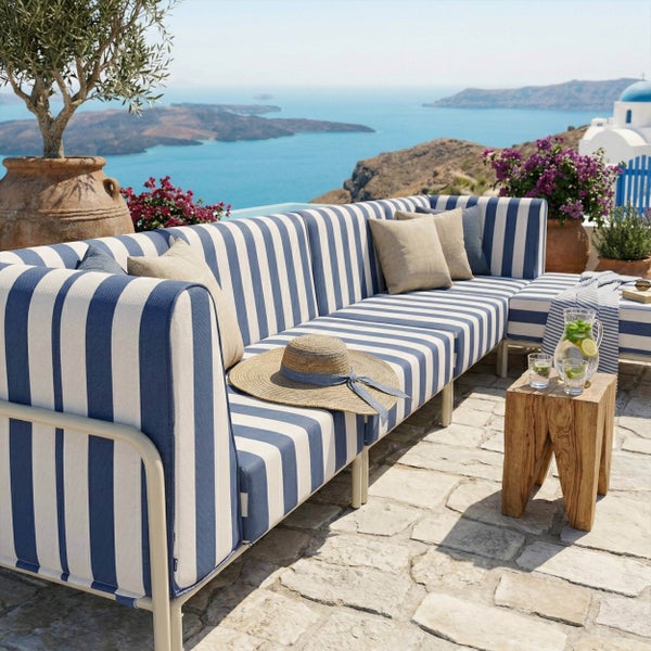 Gestreifte blau-weiße Lounge-Eckcouch auf einer hellen Steinterrasse mit Meerblick, Holzbeistelltisch und dekorativen Kissen.