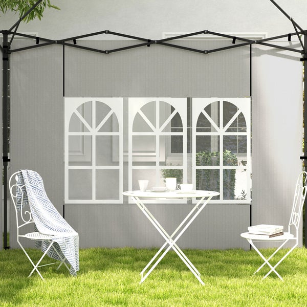 Graue Pavillon-Seitenwand mit drei Bogenfenstern hinter einem weißen Metall-Bistro-Set auf einer Rasenfläche.