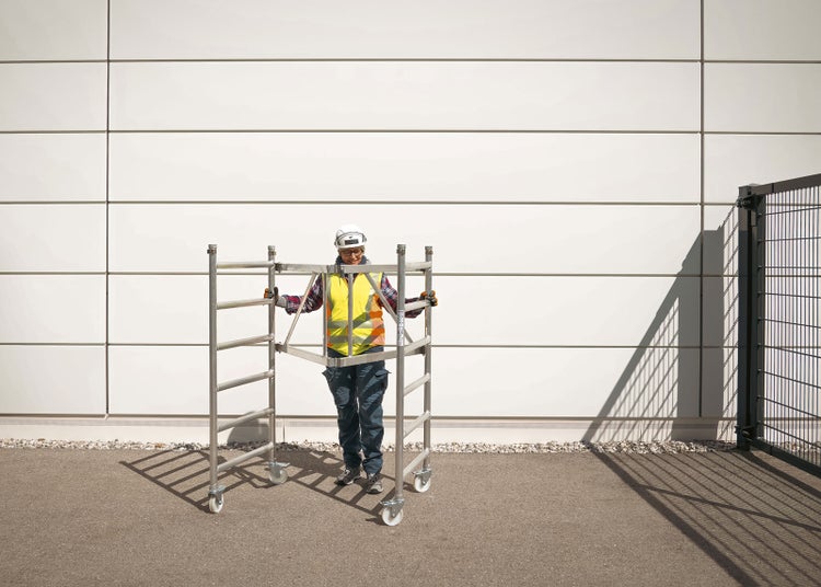 Eine Person schiebt ein fahrbares Gerüst vor einer Fassade.