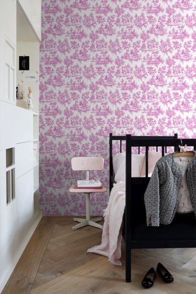 Kinderzimmer mit Toile-de-Jouy-Tapete mit rosa Landschaftsmuster, schwarzem Bett, rosa Stuhl und Fischgrätparkett.