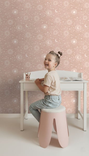 Kind am Schreibtisch in einem Zimmer mit Tapete mit Sonnen, Monden und Sternen.