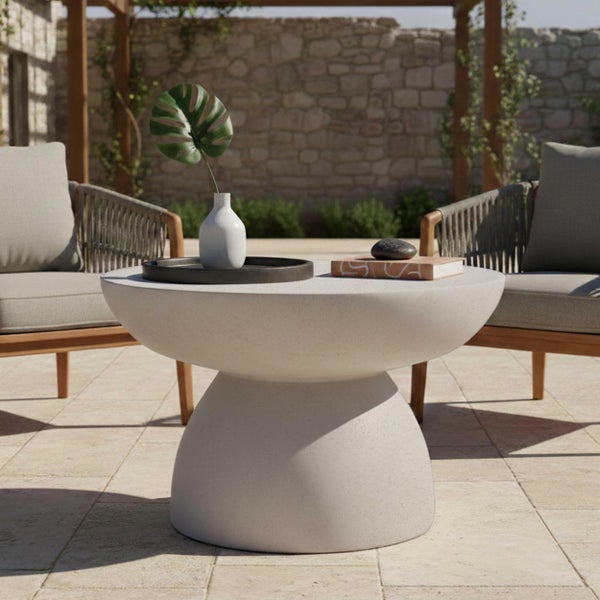 Moderner runder Beistelltisch aus Beton auf einer hellen Terrasse zwischen zwei Loungesesseln vor einer Steinmauer.