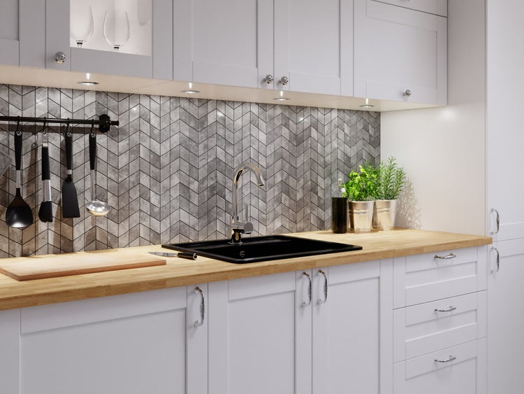 Moderne Küche mit weißen Schränken, Holzarbeitsplatte, schwarzer Spüle und grauem Fliesenspiegel mit Chevron-Muster.