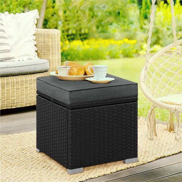 Geflochtener Gartenhocker mit Kissen, auf dem eine Tasse Kaffee und Gebäck stehen.