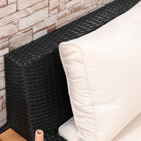 Detailaufnahme eines dunklen Gartensofas aus Polyrattan mit hellem Rückenpolster vor einer Wand in Steinoptik.