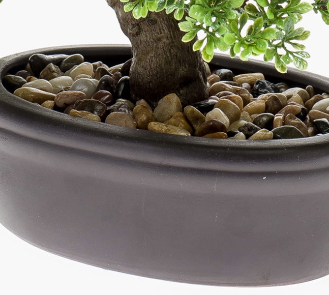 Künstlicher Bonsai in einem ovalen, anthrazitfarbenen Topf mit dekorativen Flusssteinen.
