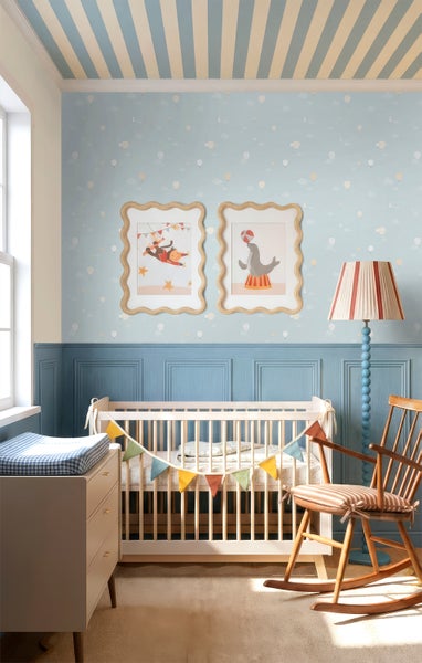 Hellblaues Kinderzimmer mit Mustertapete, blauer Wandtäfelung, weißem Gitterbett aus Holz mit Girlande und hölzernem Schaukelstuhl.