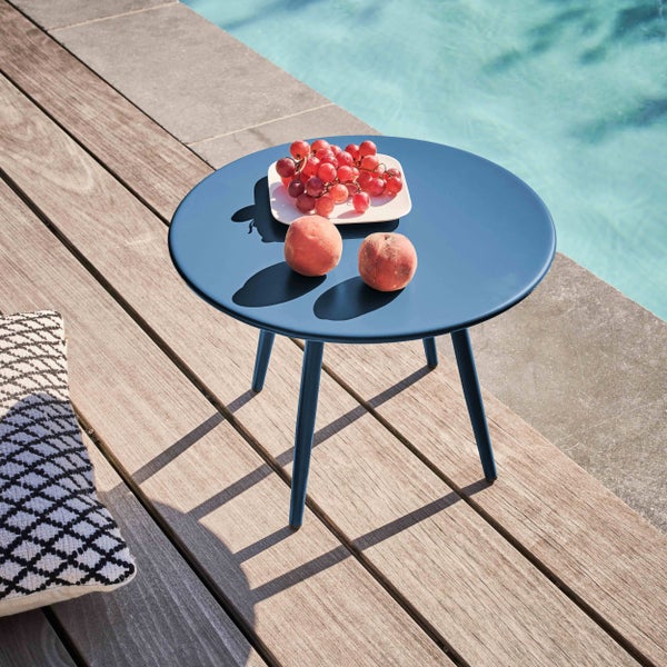 Runder Beistelltisch aus blauem Metall auf einer Holzterrasse neben einem Pool, dekoriert mit Weintrauben und Pfirsichen.