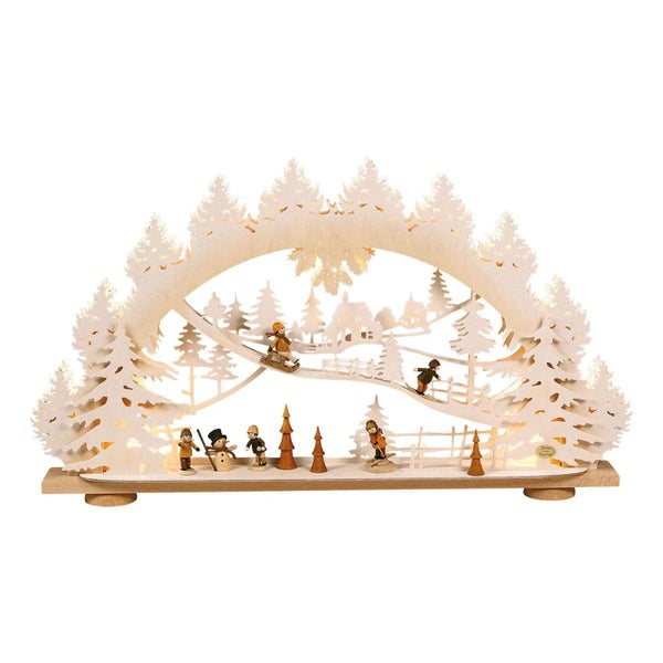 Beleuchteter Schwibbogen aus Holz mit winterlicher Szene, spielenden Figuren und Tannenbäumen als weihnachtliche Dekoration.