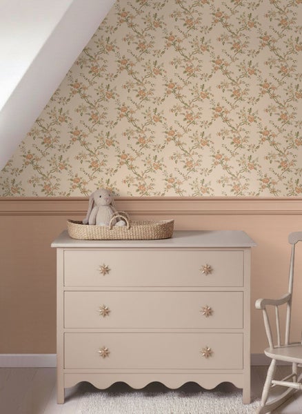 Florale Tapete mit Blumenmuster in einem Kinderzimmer über einer Wandvertäfelung mit einer Kommode und einem Schaukelstuhl.