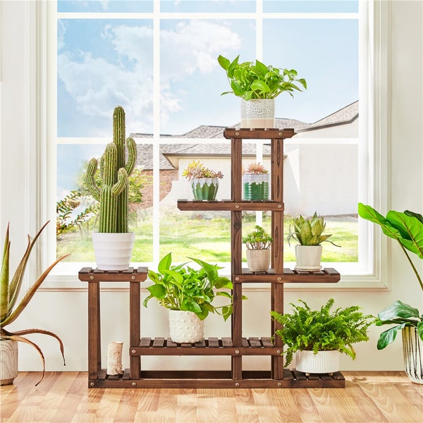 Mehrstöckiger Pflanzenständer aus Holz mit verschiedenen Topfpflanzen vor einem Fenster.