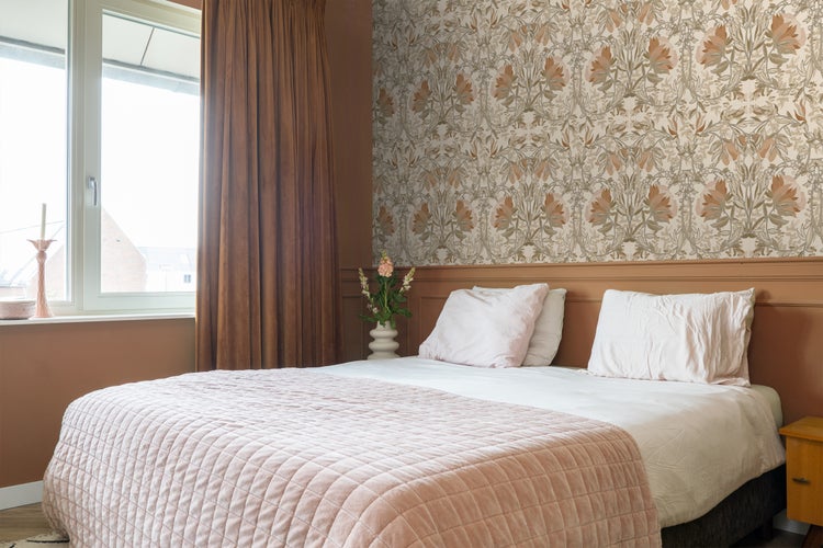 Schlafzimmer mit Bett, Nachttisch, Vorhängen und gemusterter Tapete