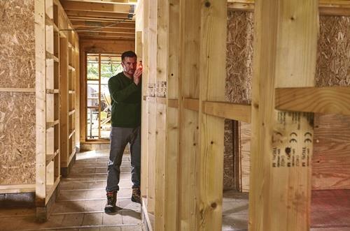 Mann mit Laser-Wasserwaage in einem Rohbau mit Holzrahmen