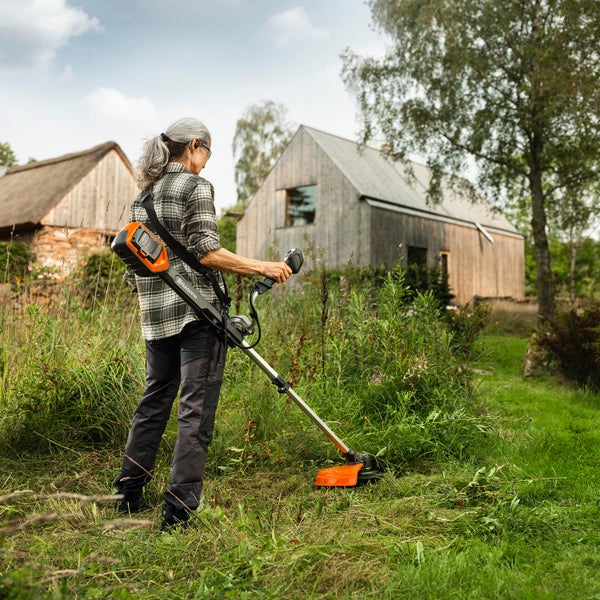 Frau benutzt Akku-Rasentrimmer von Husqvarna im Garten