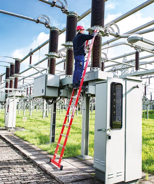 Ein Mann arbeitet auf einer roten Leiter an einer elektrischen Anlage im Freien.