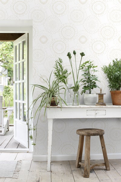 Heller Raum mit gemusterter Tapete, Tisch, Hocker und Pflanzen