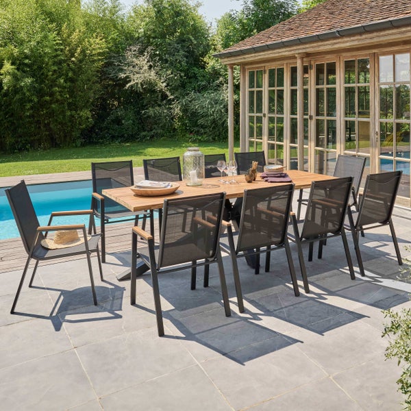 Moderne Gartensitzgruppe mit großem Holztisch und zehn schwarzen Stapelstühlen auf einer Steinterrasse neben einem Pool im Garten.