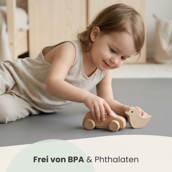 Kind spielt auf einer Matte mit Holzspielzeug in Form eines Autos und eines Vogels. Frei von Bisphenol A und Phthalaten.