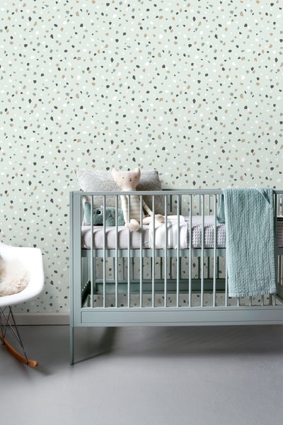 Babyzimmer mit Kinderbett, Kissen, Stofftieren und Terrazzo-Tapete