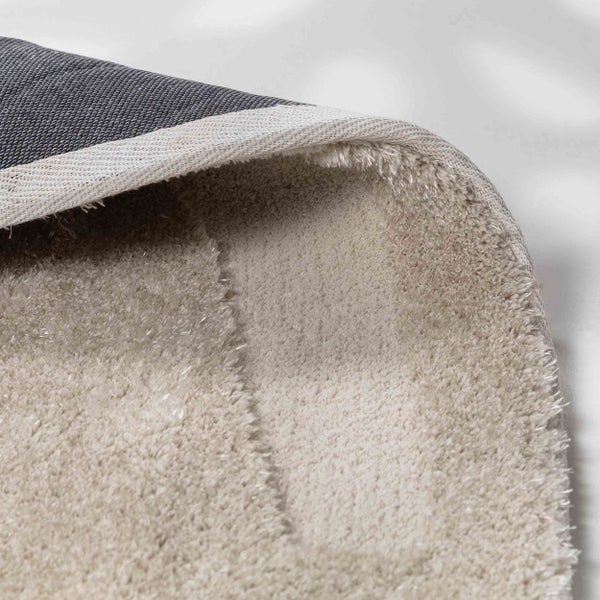 Nahaufnahme eines beigen Hochflor-Teppichs mit weicher Textur und grauem gewebtem Rücken.