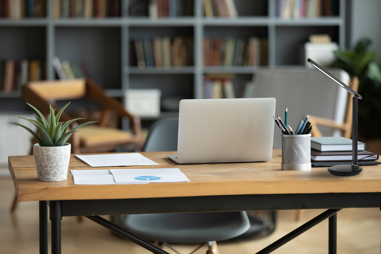 Schwarze LED-Schreibtischleuchte auf einem Holzschreibtisch in einem Arbeitszimmer mit Laptop, Pflanze und Bücherregal im Hintergrund.