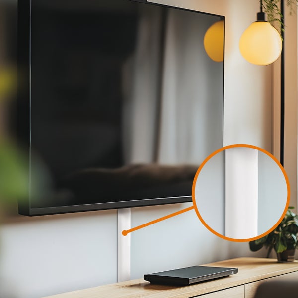 Ein weißer Kabelkanal zur diskreten Kabelführung unter einem an der Wand montierten Fernseher in einem Wohnraum.