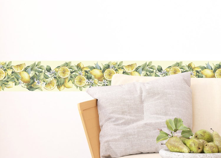 Wandbordüre mit Zitronenmuster, Blättern und Blüten an einer Wand über einem Sofa mit Kissen.