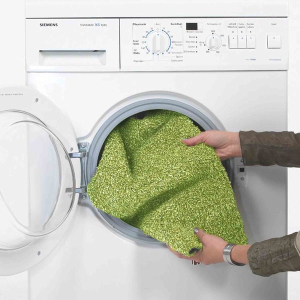 Eine grüne Badematte wird in eine Waschmaschine gelegt
