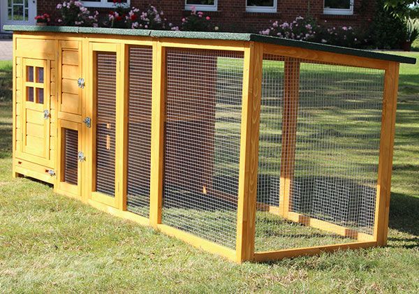 Heller Kleintierstall aus Holz mit integriertem Freigehege aus Drahtgeflecht und geneigtem Dach in einem Garten.