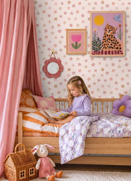 Kinderspielzimmer mit geblümter Tapete, einem Holzbet mit Baldachin, gemusterter Bettwäsche, Wandbildern, einem Spiegel und Spielzeug.