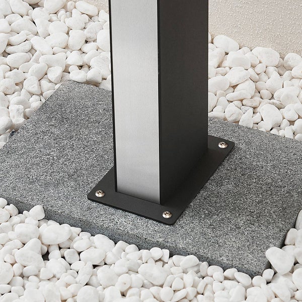 Sockel einer rechteckigen Außenleuchte mit schwarzer Bodenplatte, befestigt auf einer grauen Granitplatte inmitten von weißem Zierkies.