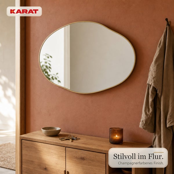 Ovaler Wandspiegel mit schmalem Rahmen in einem Flur mit Holzkommode, Kerze und Garderobe. Karat Logo.