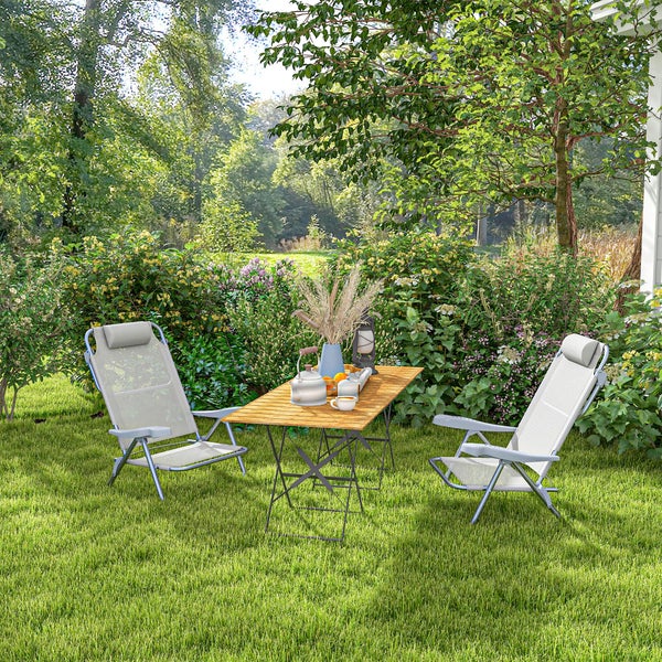 Helle Gartenszene mit zwei Klappsesseln und einem Holztisch mit Metallgestell auf einer Rasenfläche, umgeben von Blumen und Bäumen.