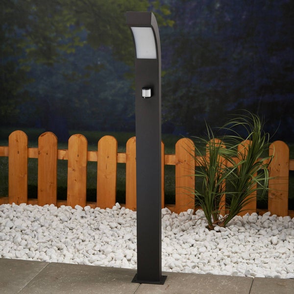 Moderne schwarze Wegeleuchte mit Bewegungsmelder im Garten neben einem Holzzaun und weißen Kieselsteinen.