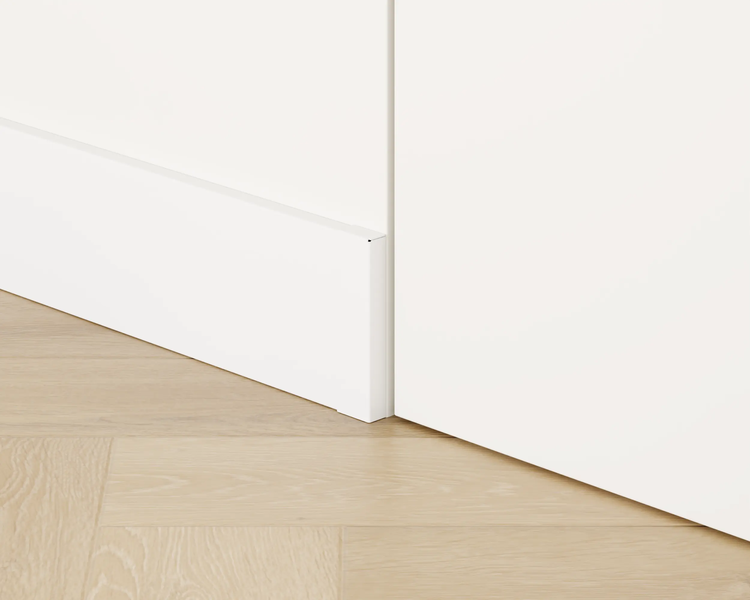 Detailansicht eines weißen Schranks mit Sockelleiste auf einem hellen Holzboden