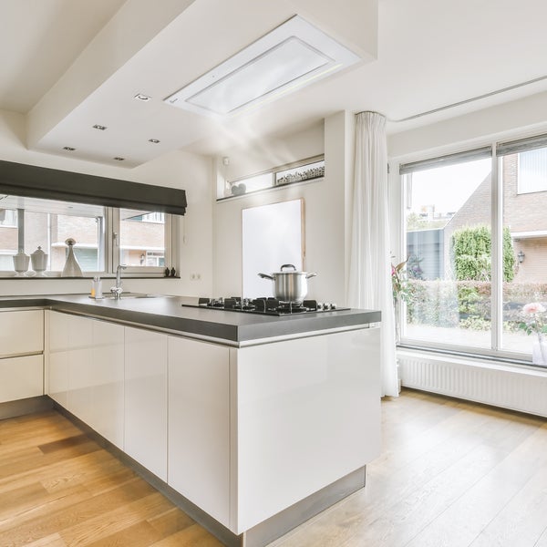 Helle, moderne Küche mit weißer Kochinsel, dunkler Arbeitsplatte und Decken-Dunstabzug über einem Gaskochfeld mit Edelstahltopf.