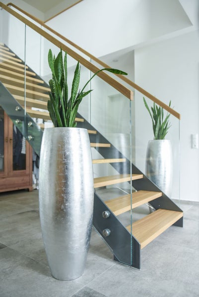 Große silberne Bodenvasen mit Bogenhanf neben einer modernen Treppe mit Holzstufen und Glasgeländer.
