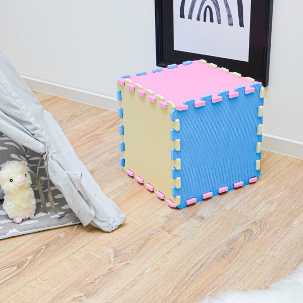 Würfel aus zusammengesteckten Schaumstoff-Puzzlematten in einem hellen Kinderzimmer neben einem Spielzelt auf Holzboden.