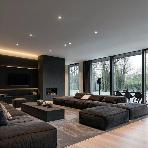 Modernes, geräumiges Wohnzimmer mit dunklem modularem Sofa, niedrigem Couchtisch, Kamin, beleuchteter TV-Wand und großen Fensterfronten.
