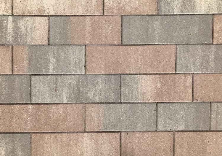 Rechteckige Pflastersteine aus Beton mit strukturierter Oberfläche in Grau- und Brauntönen.