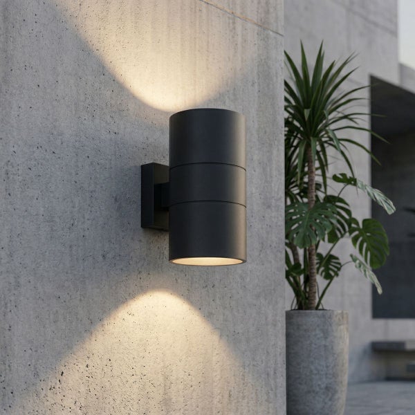 Schwarze Außenwandleuchte in Zylinderform an einer Betonwand mit Lichtkegeln nach oben und unten.
