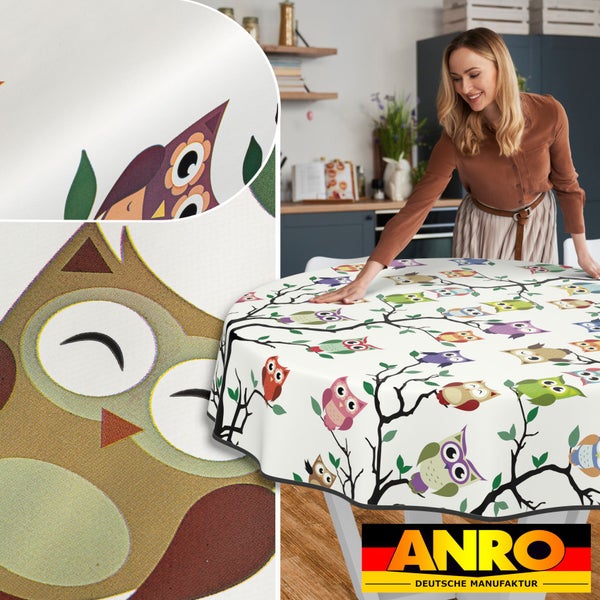 Frau drapiert runden Tisch mit ANRO Wachstuchtischdecke mit Eulenmotiven in der Küche.