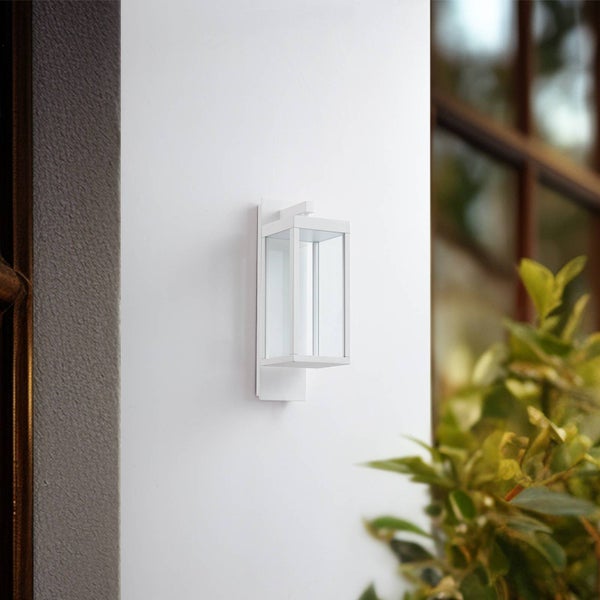 Moderne Außenwandleuchte mit weißem Metallrahmen und klaren Glasfenstern, an einer Hauswand montiert.