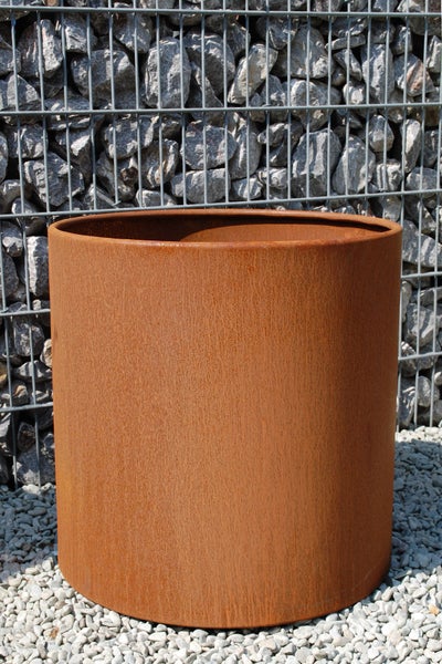 Zylindrischer Pflanzkübel aus Corten-Stahl mit Rostoptik vor einer Gabionenwand auf Kies.