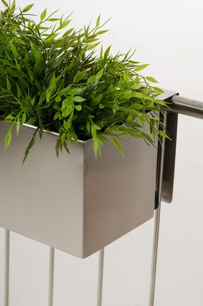 Quadratischer Blumenkasten aus Edelstahl mit grünen Kunstpflanzen an einem Metallgeländer.